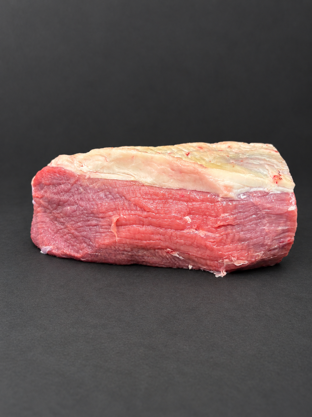 Side view of beef roasting joint on a smooth charcoal background