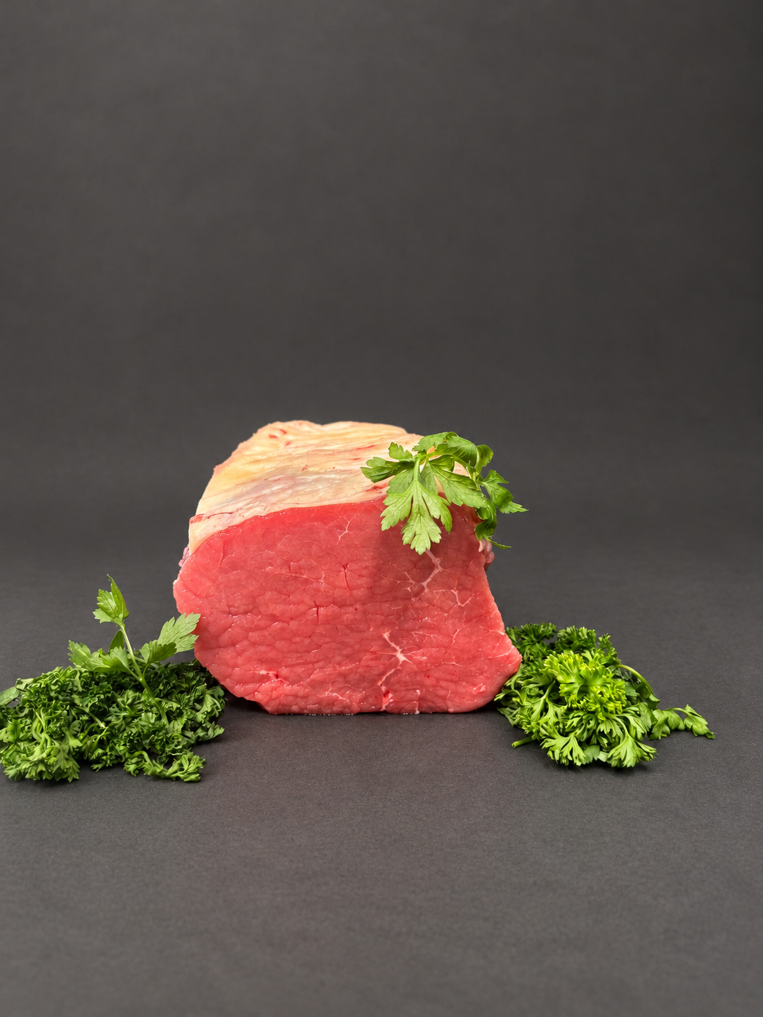 Beef roasting joint with parsley on a smooth charcoal background